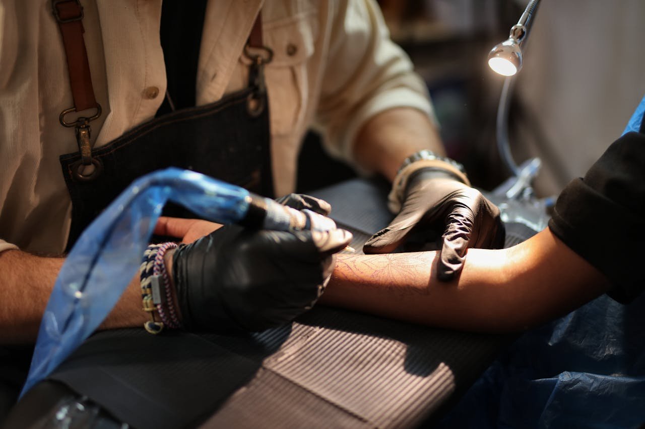 A tattoo artist concentrates as they create intricate designs on a client's arm in studio lighting.
